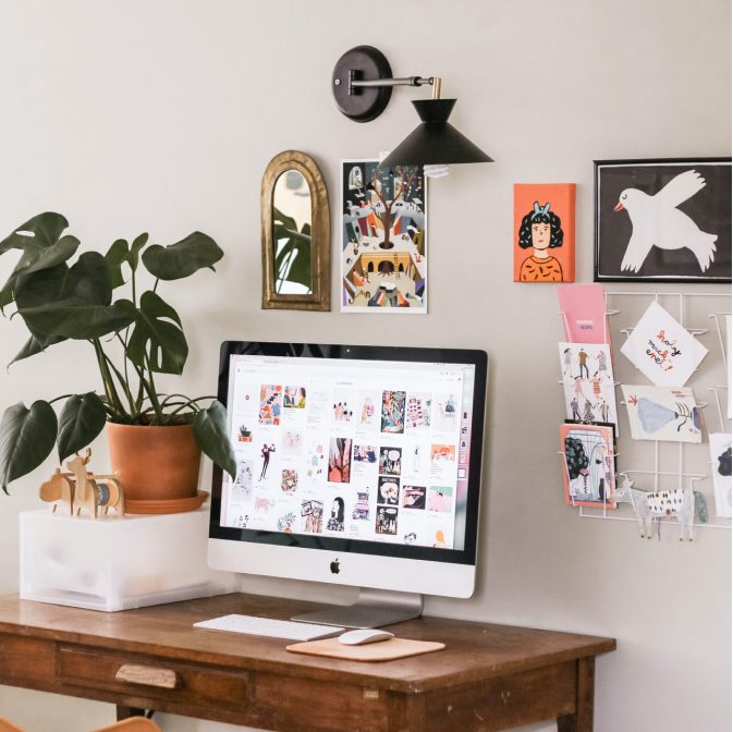 A table with iMac device on top of it, plant next to it