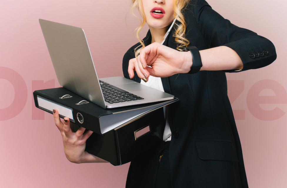 A woman in a suit talking on a mobile phone while holding a laptop and file case