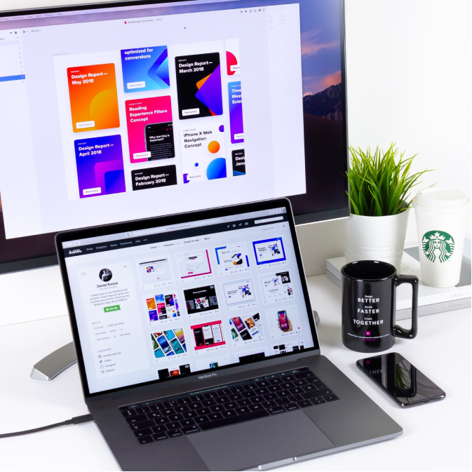 MacBook laptop on white table with a phone, a mug and a monitor