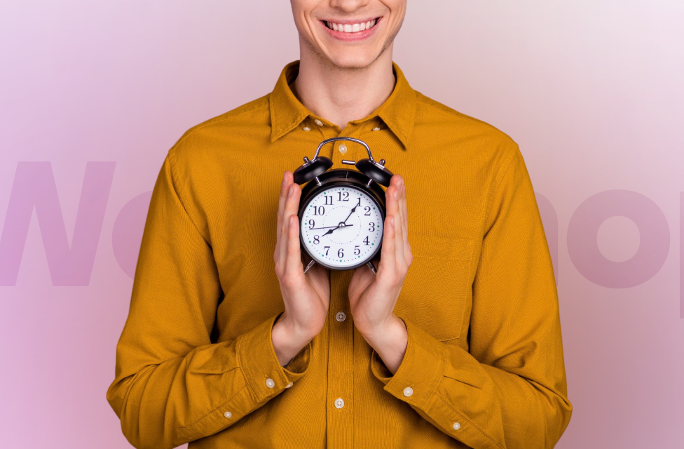 A young man in a yellow shirt is holding an alarm clock